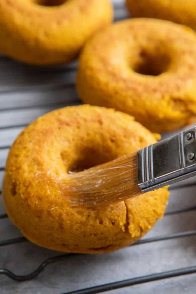 Brushing melted butter on donut with a pastry brush.