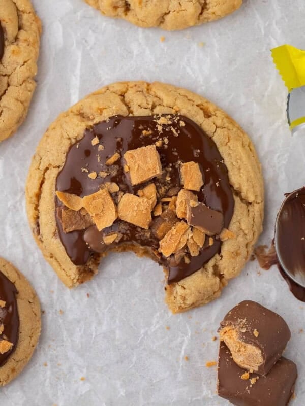 Bitten Crumbl Butterfinger cookie topped with melted chocolate and Butterfinger pieces on parchment paper