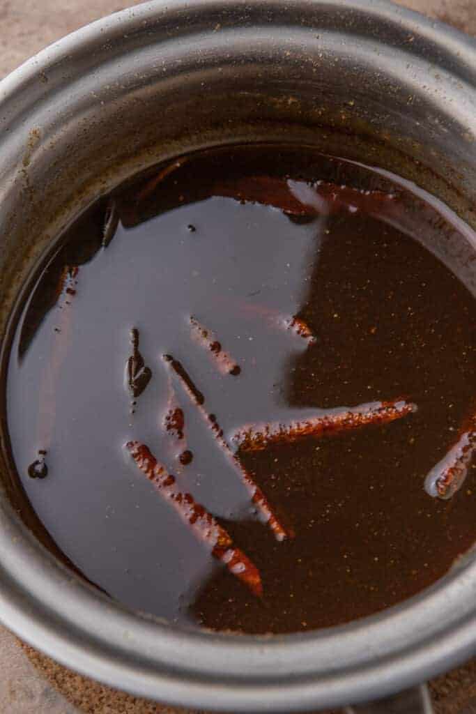 Thickened pumpkin spice syrup simmering in the pan and coating the back of a spoon.