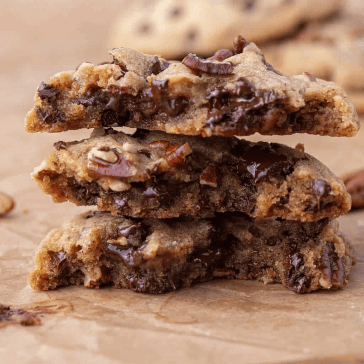 Stack of brown butter pecan chocolate chip cookies broken in half, showing gooey melted chocolate chips and toasted pecan pieces on parchment paper.
