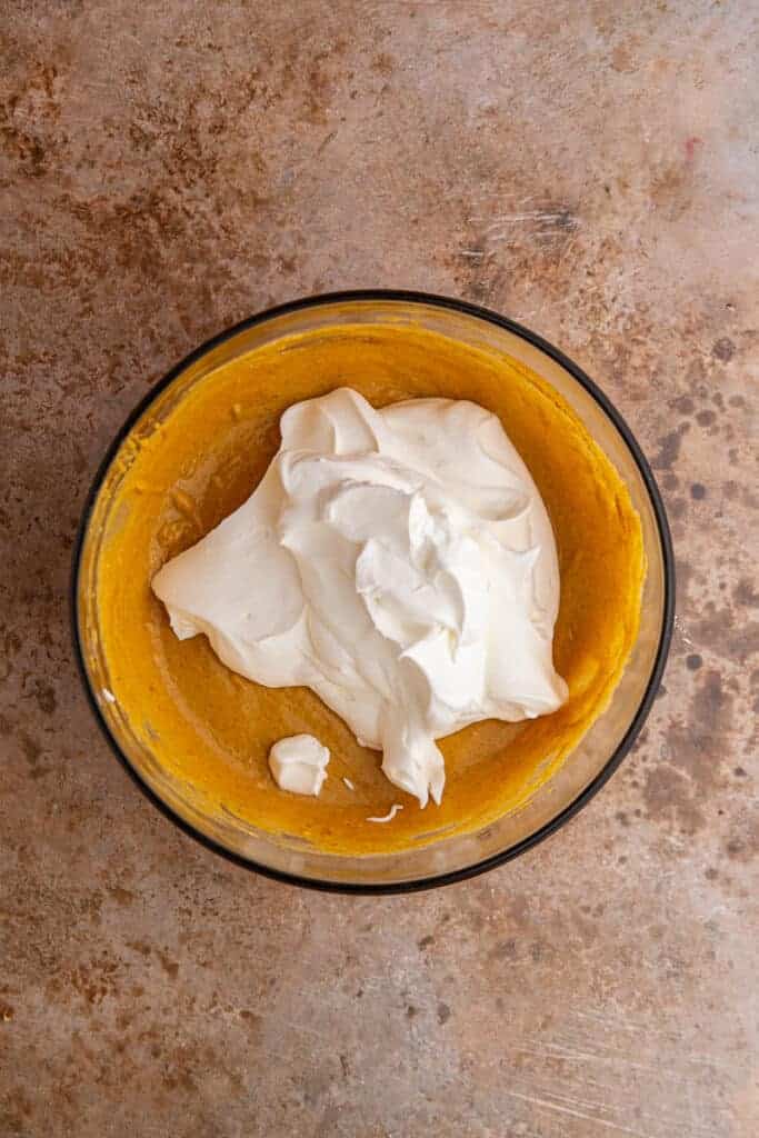 Whipped cream spooned over the spiced pumpkin mixture before folding the two together gently.