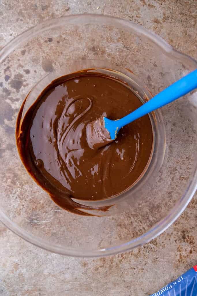 Finished muddy buddies spread out on parchment paper to set, fully coated in powdered sugar and mixed with cookies and candies.
