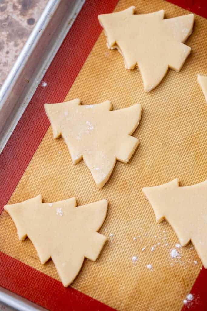 Unbaked Christmas tree-shaped sugar cookies on a baking tray lined with silicone mat.