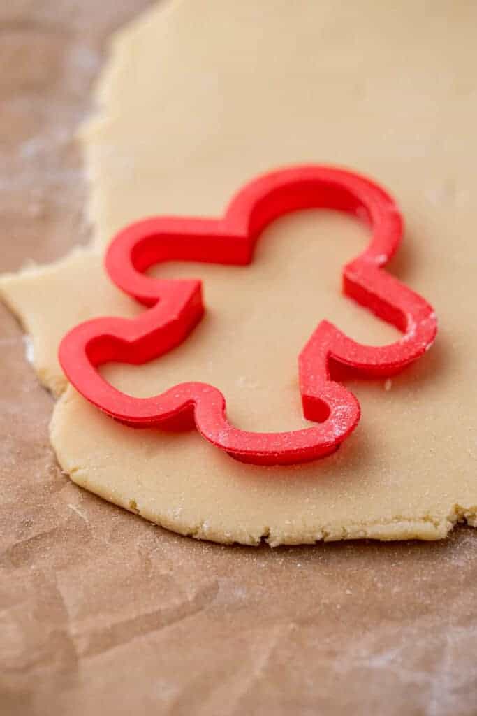 Red gingerbread man cookie cutter pressed into sugar cookie dough on parchment paper.