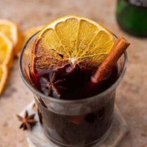 French vin chaud in a glass mug garnished with a dried orange slice, cinnamon stick and star anise.