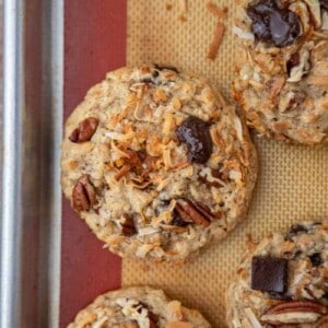 Overhead view of baked cowboy cookies with chocolate chunks, pecans and toasted coconut on a lined baking sheet.