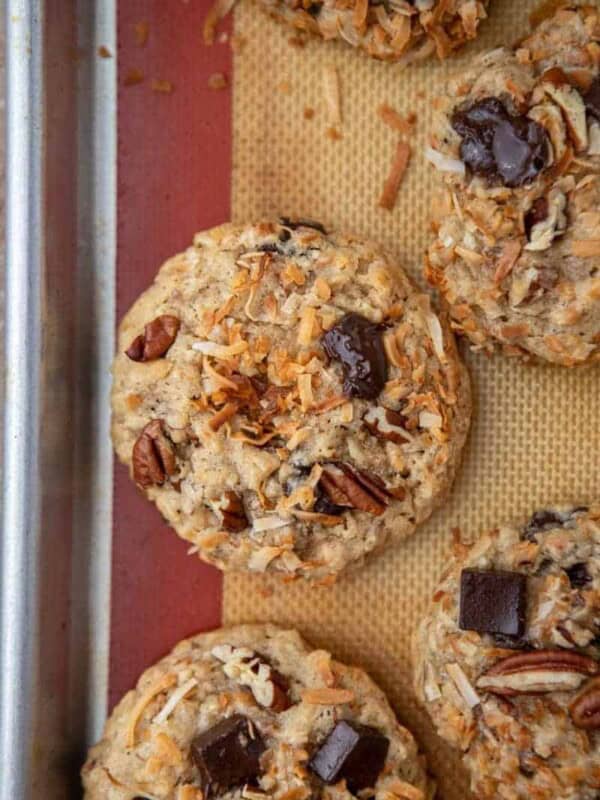 Overhead view of baked cowboy cookies with chocolate chunks, pecans and toasted coconut on a lined baking sheet.