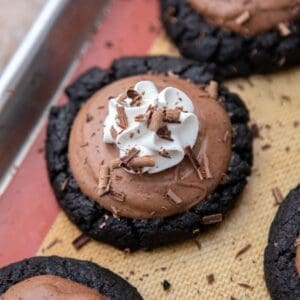 Crumbl French silk pie cookies on a baking sheet, topped with chocolate mousse, whipped cream, and chocolate shavings.