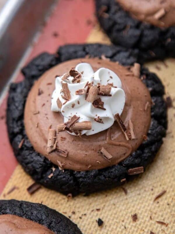 Crumbl French silk pie cookies on a baking sheet, topped with chocolate mousse, whipped cream, and chocolate shavings.