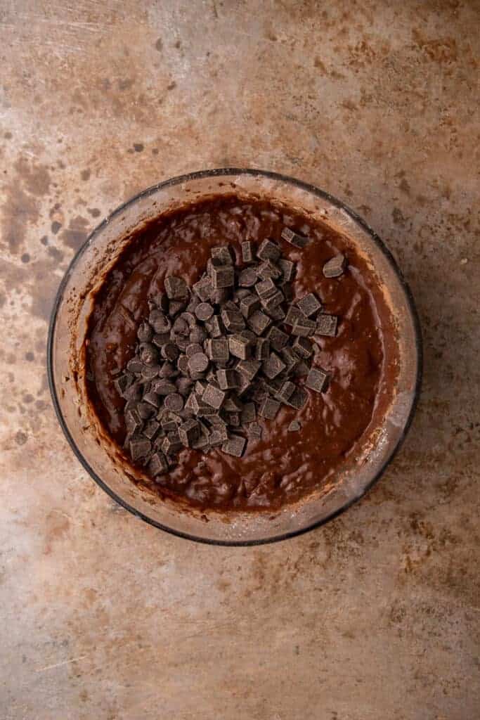 Rich chocolate batter in a glass bowl topped with chocolate chunks ready to be folded in