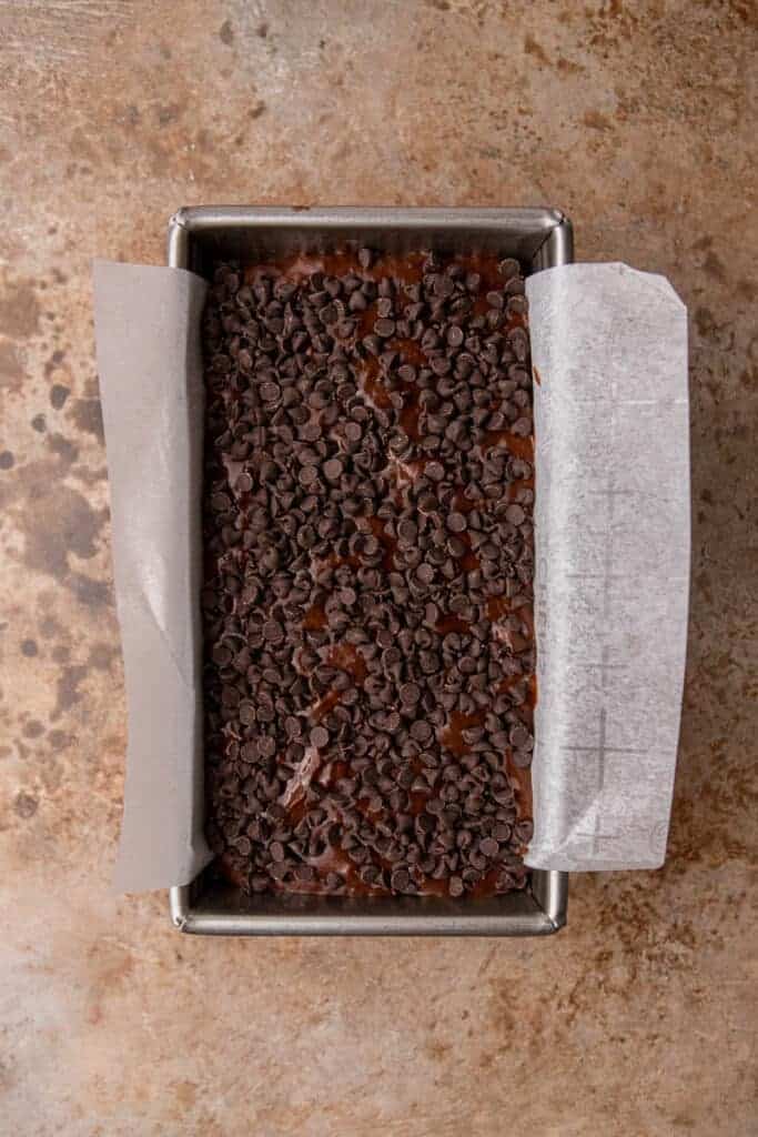 Unbaked batter poured into a parchment-lined loaf pan and covered with a generous layer of mini chocolate chips before going into the oven