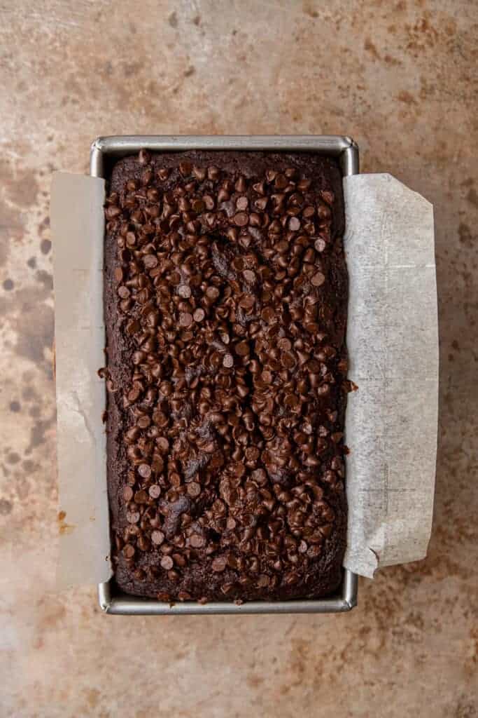 Freshly baked double chocolate banana bread in a parchment-lined loaf pan with a crackly chocolate chip crust on top