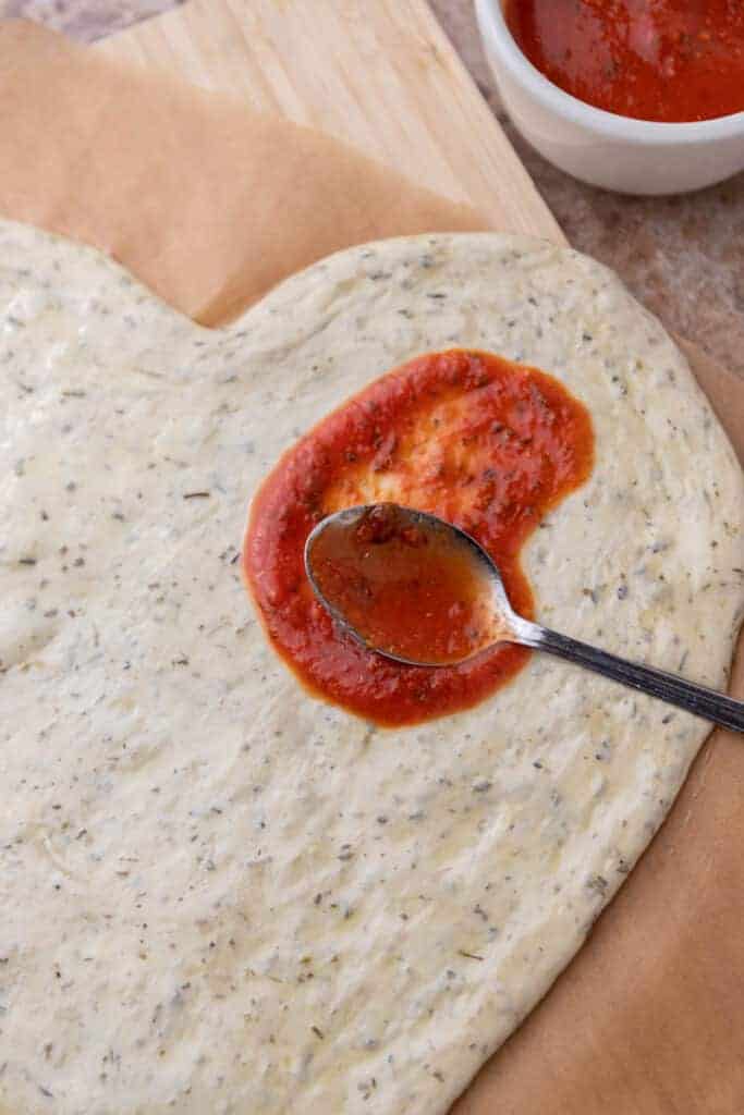Spoon spreading tomato sauce on dough