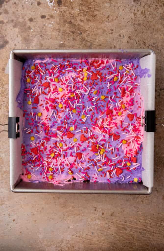 Valentine’s Day sugar cookie bars frosted with pink and purple buttercream and sprinkles