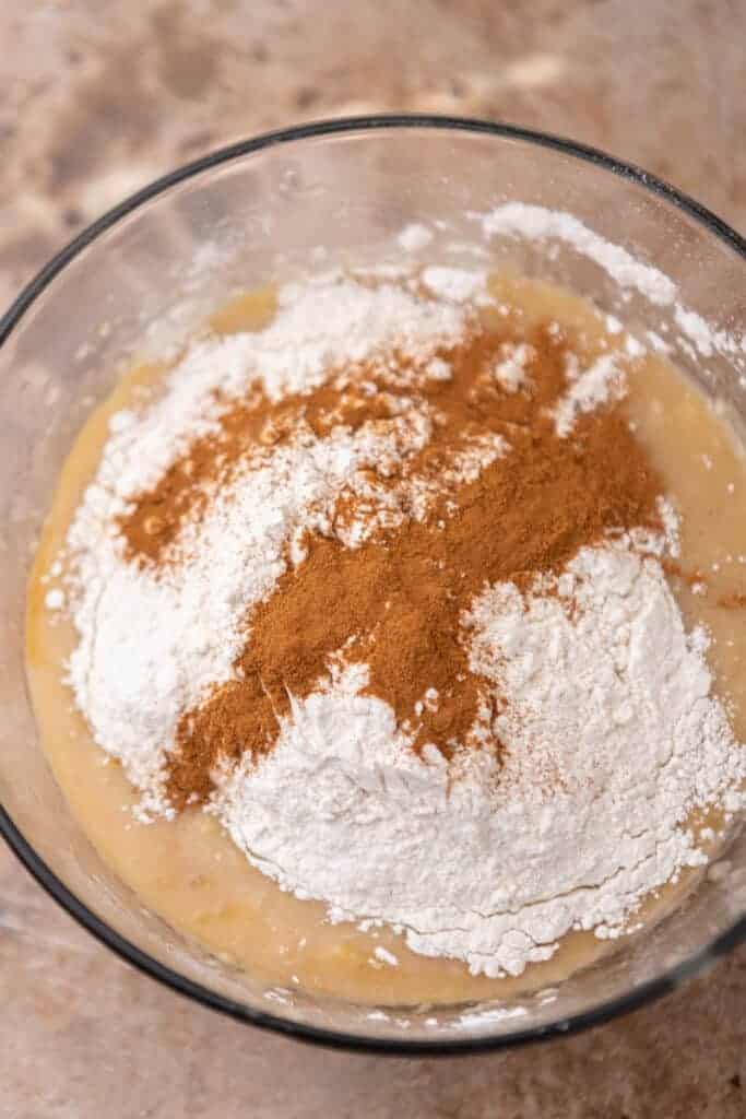 Flour and cinnamon added to wet ingredients in a bowl for eggless banana bread batter