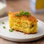 A square of cornbread with bites taken out of it, sitting on a small white plate.