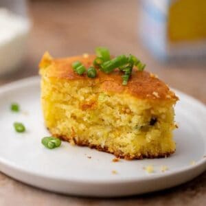 A square of cornbread with bites taken out of it, sitting on a small white plate.