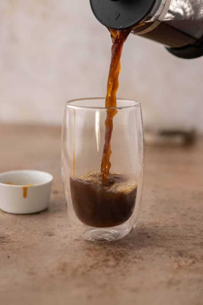Hot brewed coffee being poured over caramel sauce in a double wall glass