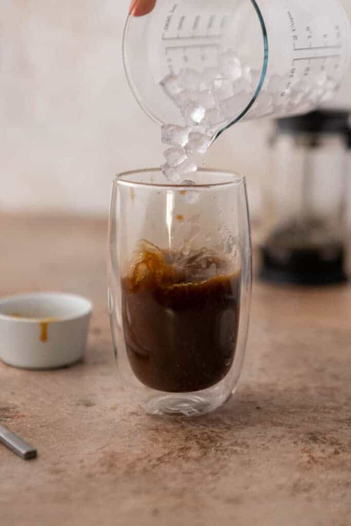 Ice cubes being added to the caramel coffee in a clear glass