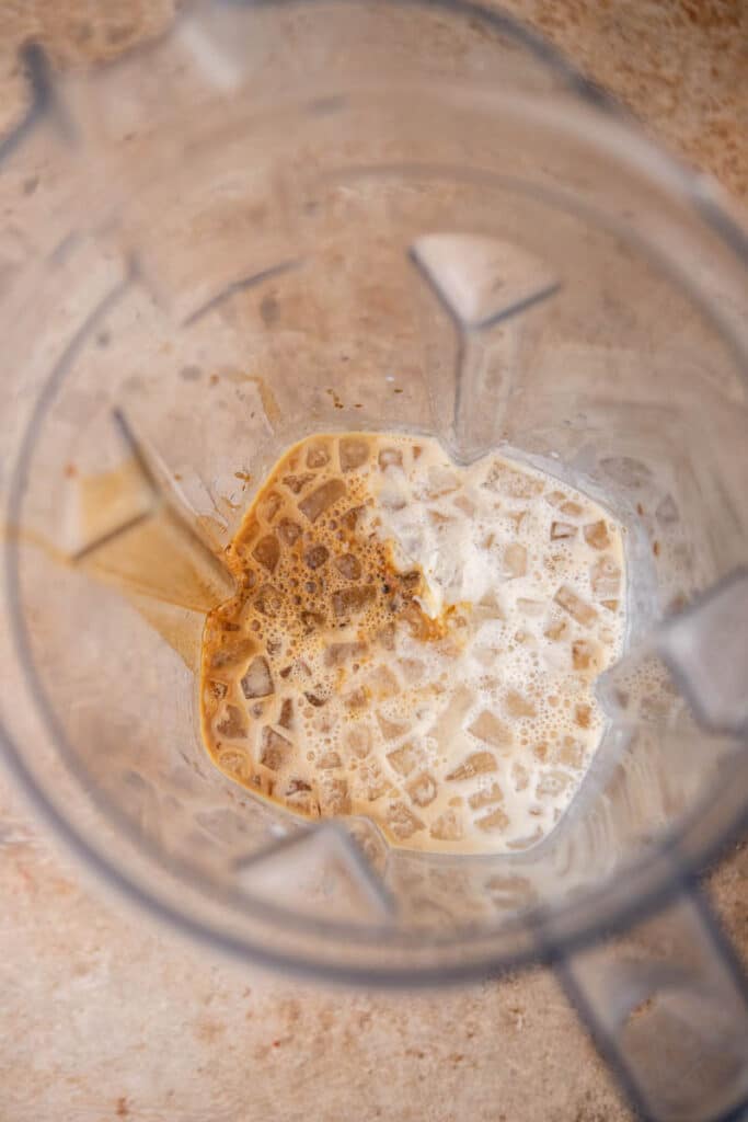 Ingredients for homemade McDonald’s caramel frappe including ice, coffee, caramel syrup, and milk in a blender before blending