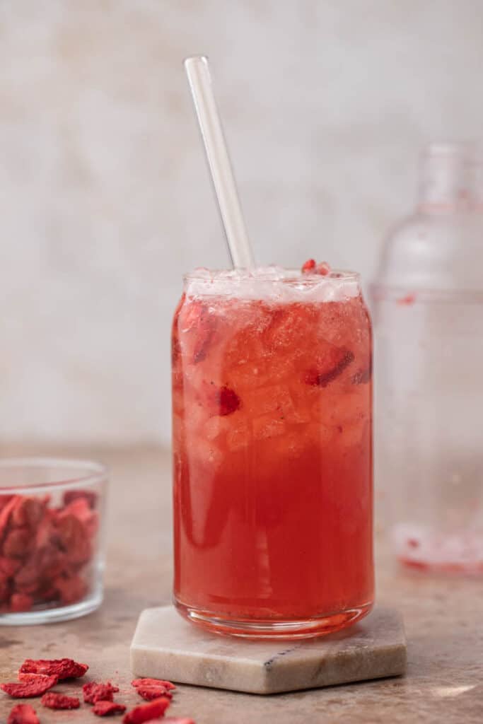 Homemade Starbucks strawberry acai refresher in a glass can cup with a glass straw and freeze dried strawberries on the side