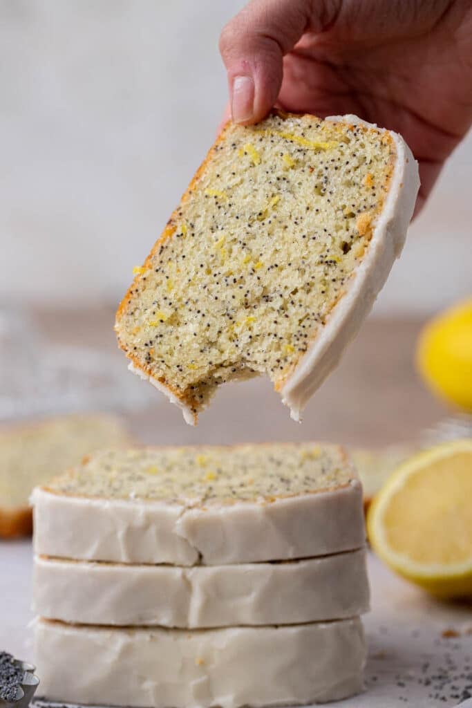 Hand holding slice of lemon poppy seed loaf cake