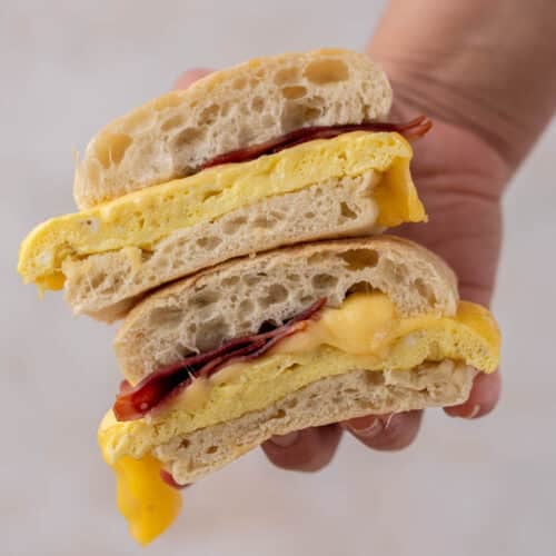 Hand holding bacon egg gouda sandwich from starbucks