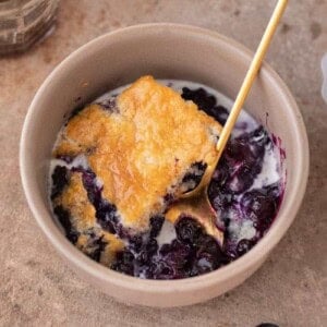 A serving of blueberry cobbler in a bowl with a gold spoon.