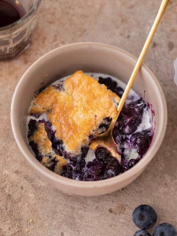 A serving of blueberry cobbler in a bowl with a gold spoon.