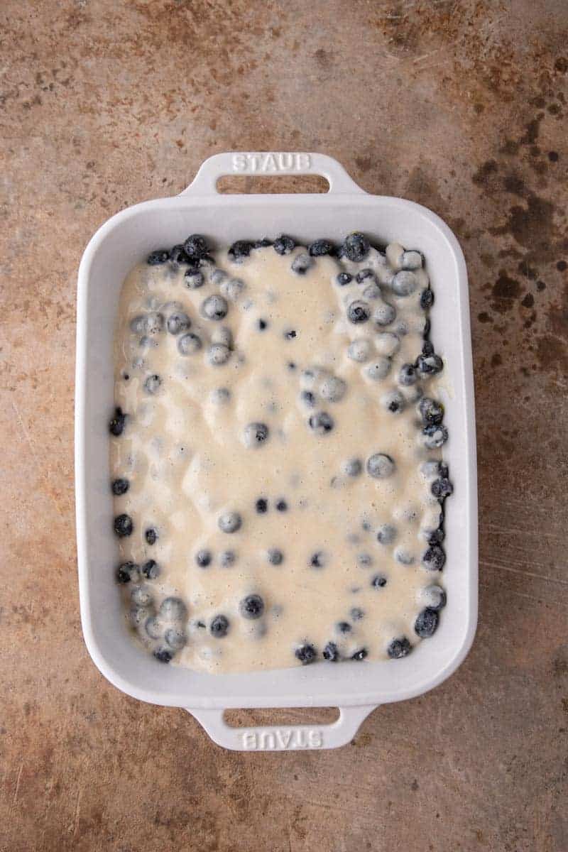 Blueberries and cobbler batter layered in a white baking dish before baking.