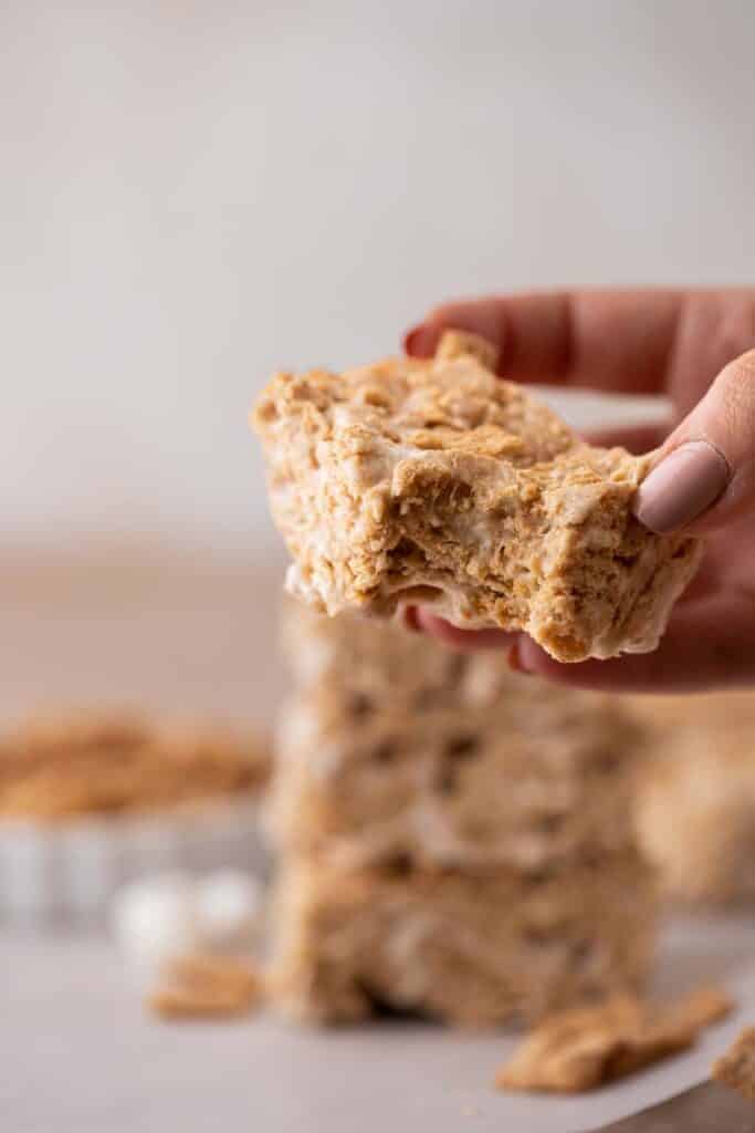 A hand holding a cinnamon toast crunch bar with a bite taken out of it.