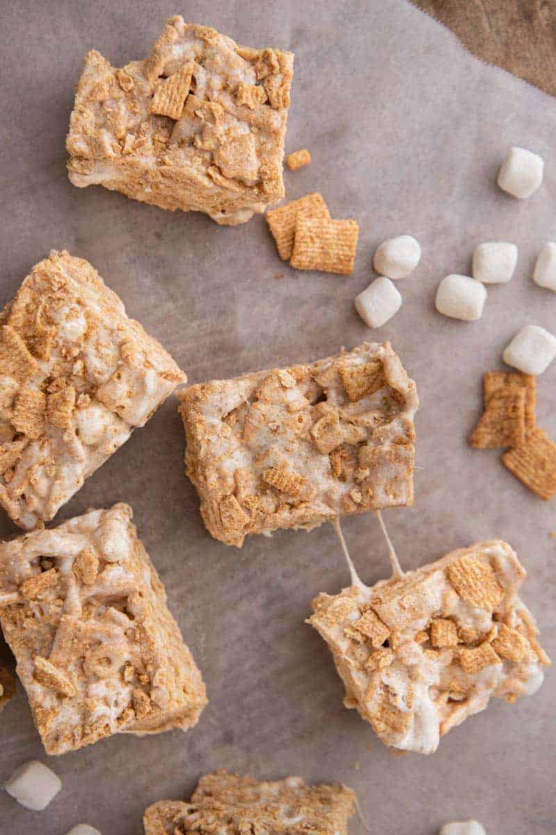 Cinnamon toast crunch bars cut into squares on parchment paper with mini marshmallows.