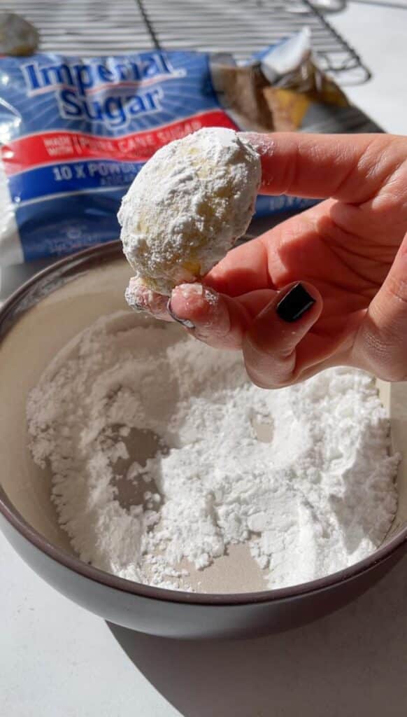 Hand dipping cookies in powdered sugar