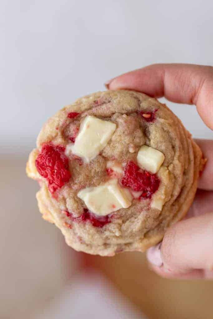 Hand holding a chewy raspberry white chocolate chip cookie with chunks of white chocolate and fresh raspberries baked in