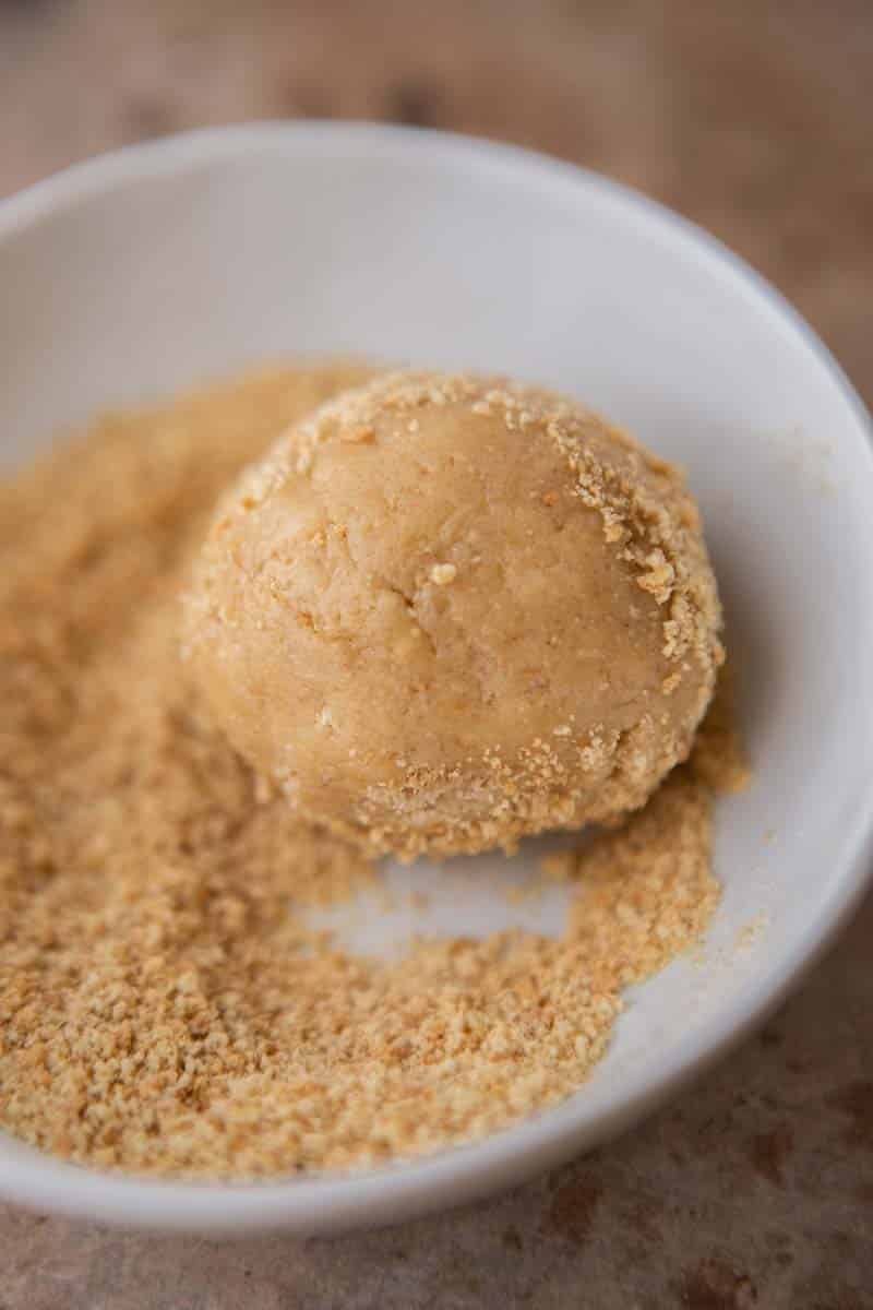 A ball of graham cracker cookie dough rolled in graham cracker crumbs in a white bowl.