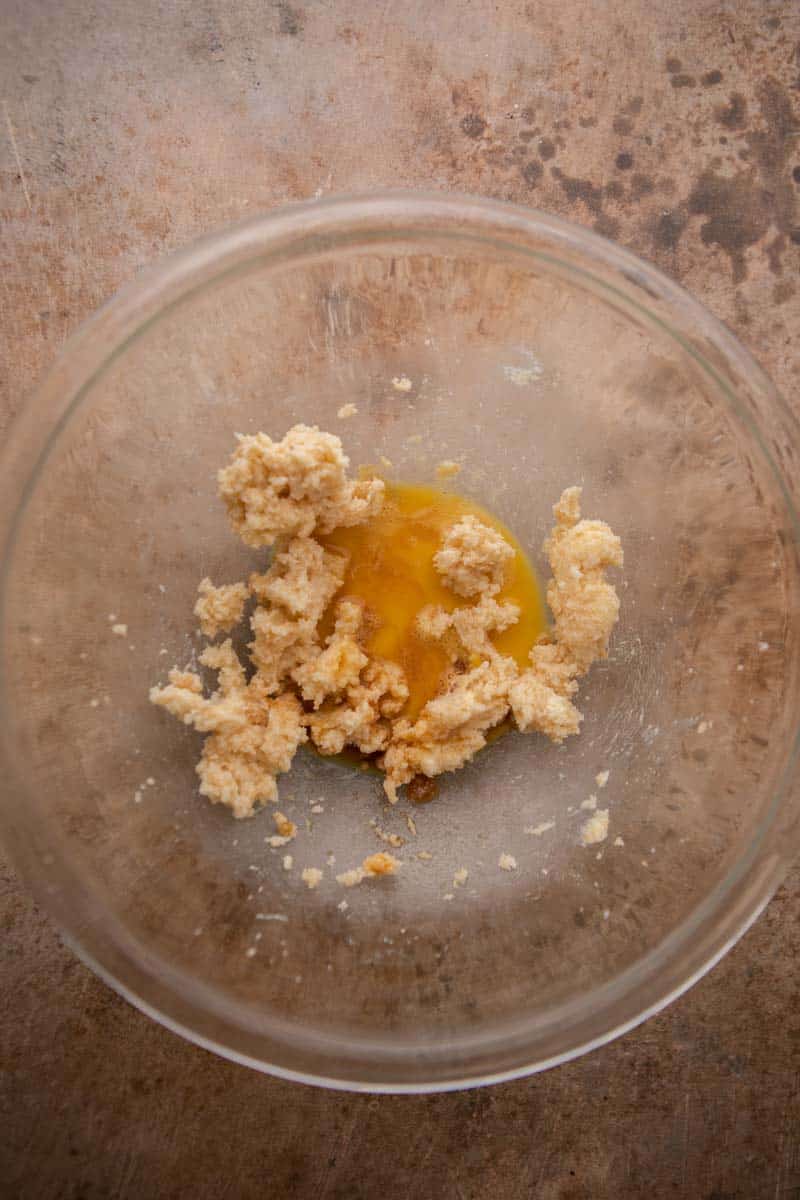Creamed butter and sugars in a glass bowl with an egg and vanilla added on top.