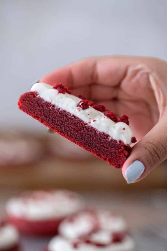 Hand holding Crumbl red velvet cookie sliced in half