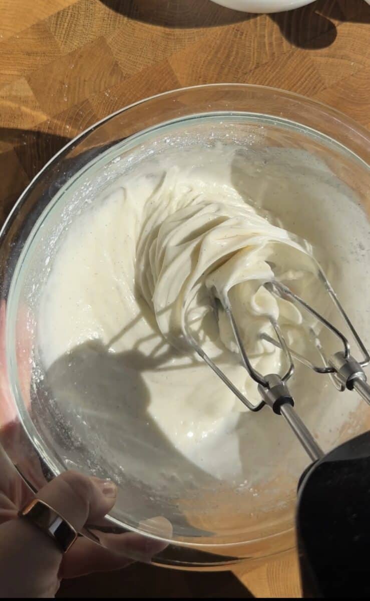 Cream cheese glaze being whipped in a glass bowl with hand mixer