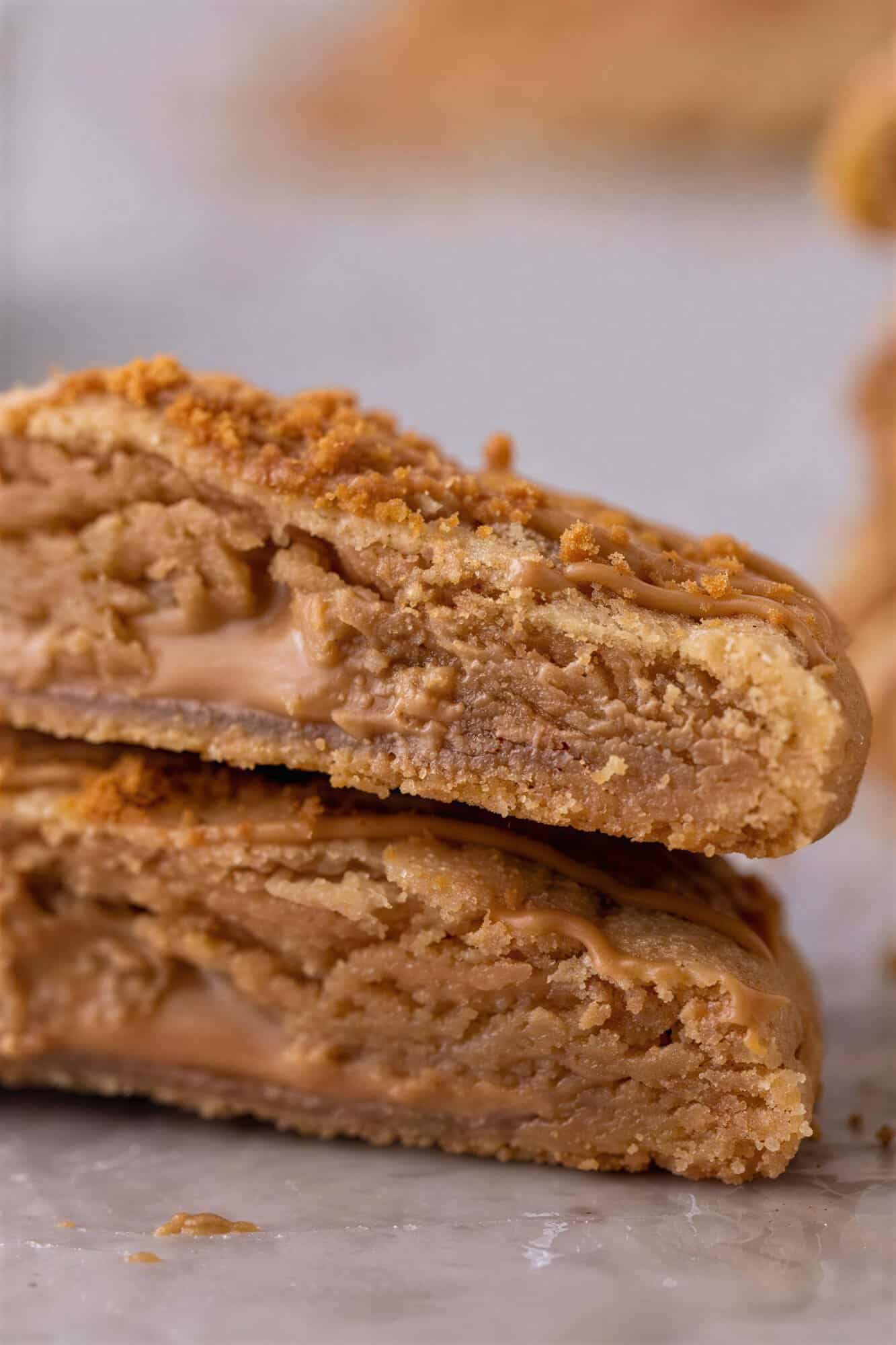 Two Biscoff lava cookies split in half and stacked showing the gooey cookie butter center.