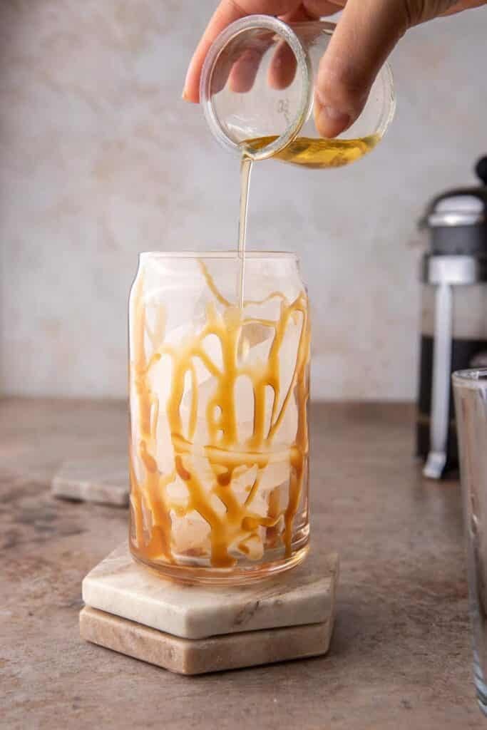 Caramel syrup being poured in a tall glass of ice