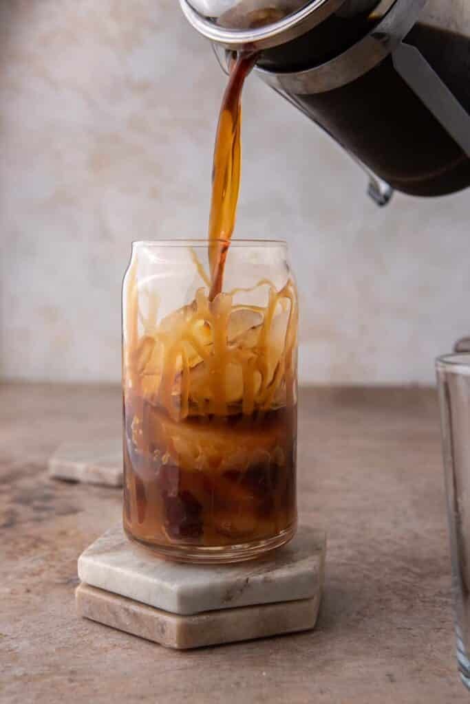 Coffee being poured in a tall glass of ice