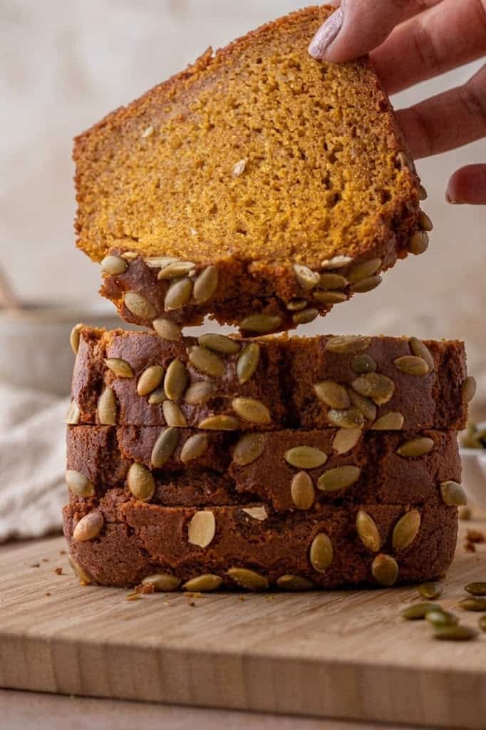 A hand holding a slice of homemade Starbucks pumpkin bread with pepitas still attached.