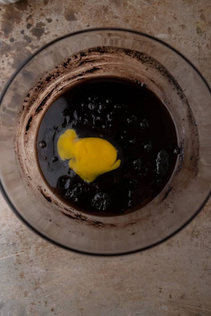 Dark cocoa batter in a bowl with an egg mixed in there