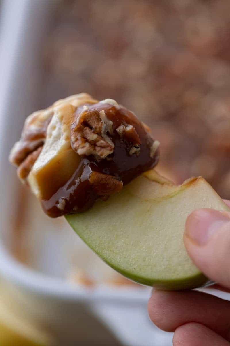 Green apple slice dipped into caramel apple cheesecake dip with pecans.