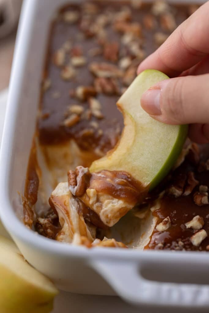 Hand dipping apple in cheesecake dip