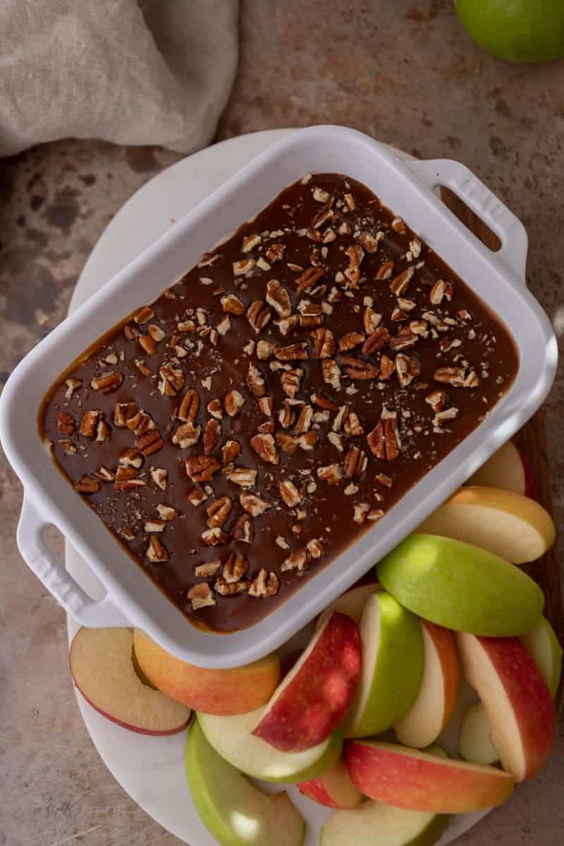 Caramel apple cheesecake dip topped with chopped pecans next to sliced apples.