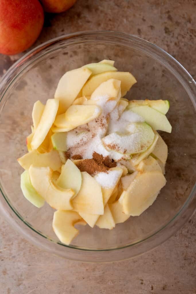 Sliced apples in a bowl with cinnamon and nutmeg