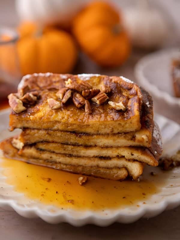 A stack of pumpkin French toast topped with chopped pecans, powdered sugar, and maple syrup.