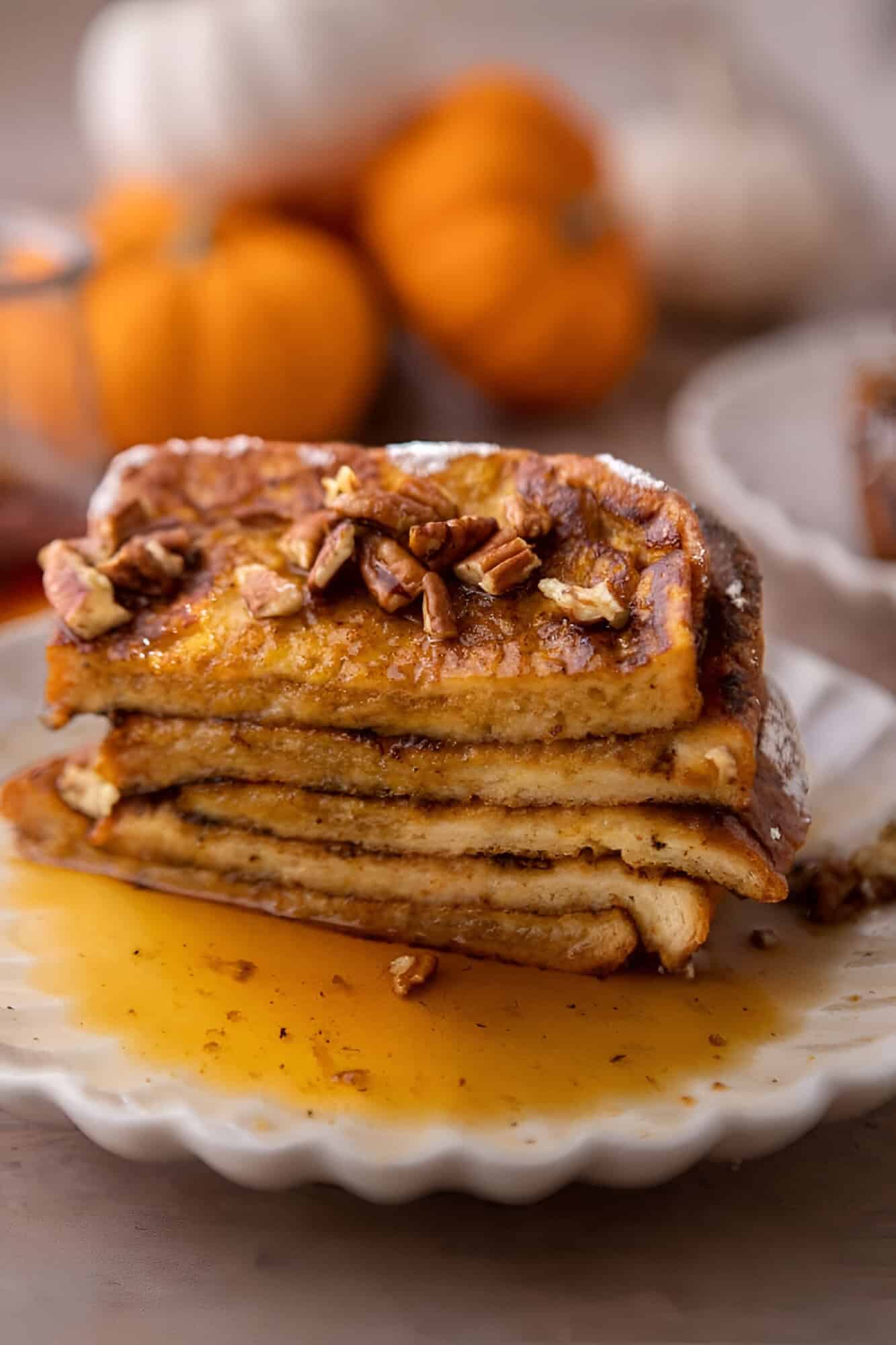 A stack of pumpkin French toast topped with chopped pecans, powdered sugar, and maple syrup.