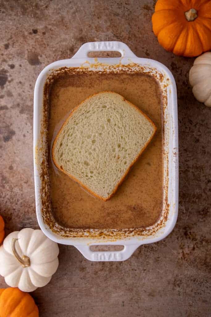 A slice of bread soaking in pumpkin custard for 30 seconds per side before cooking.